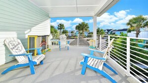 A covered outdoor area with Adirondack chairs, a wooden sign, and a view of houses and palm trees.