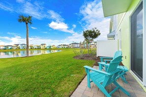 Un área junto a la piscina con sillas Adirondack turquesas, una palmera y vistas a una hilera de casas coloridas.
