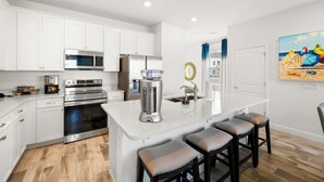 A modern kitchen with white cabinetry, stainless steel appliances, and a central island with stools. - Lime Green Villa near Disney | Margaritaville & Waterpark Access - 2965CS (Kissimmee)