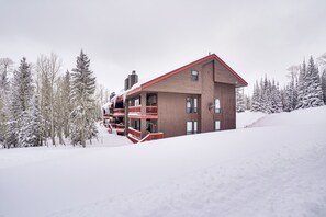 A modern wooden cabin with a red roof, multiple balconies, and a ski lift nearby.