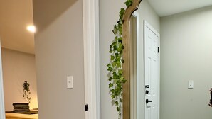 A hallway with a large mirror, wooden flooring, and a door leading to a bedroom.