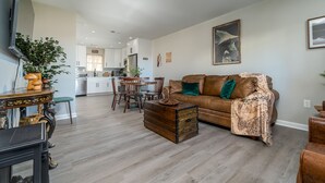 A modern living room with a brown leather sofa, a wooden chest, and a dining area with wooden chairs and a table.