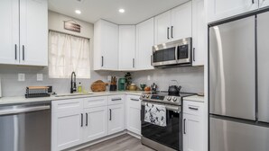 A modern kitchen with white cabinets, stainless steel appliances, and a wooden floor.