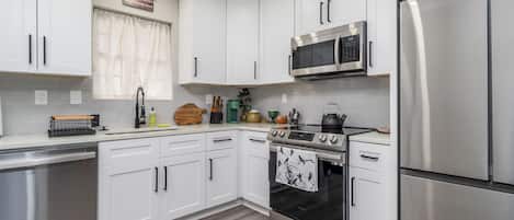 A modern kitchen with white cabinets, stainless steel appliances, and a wooden floor.