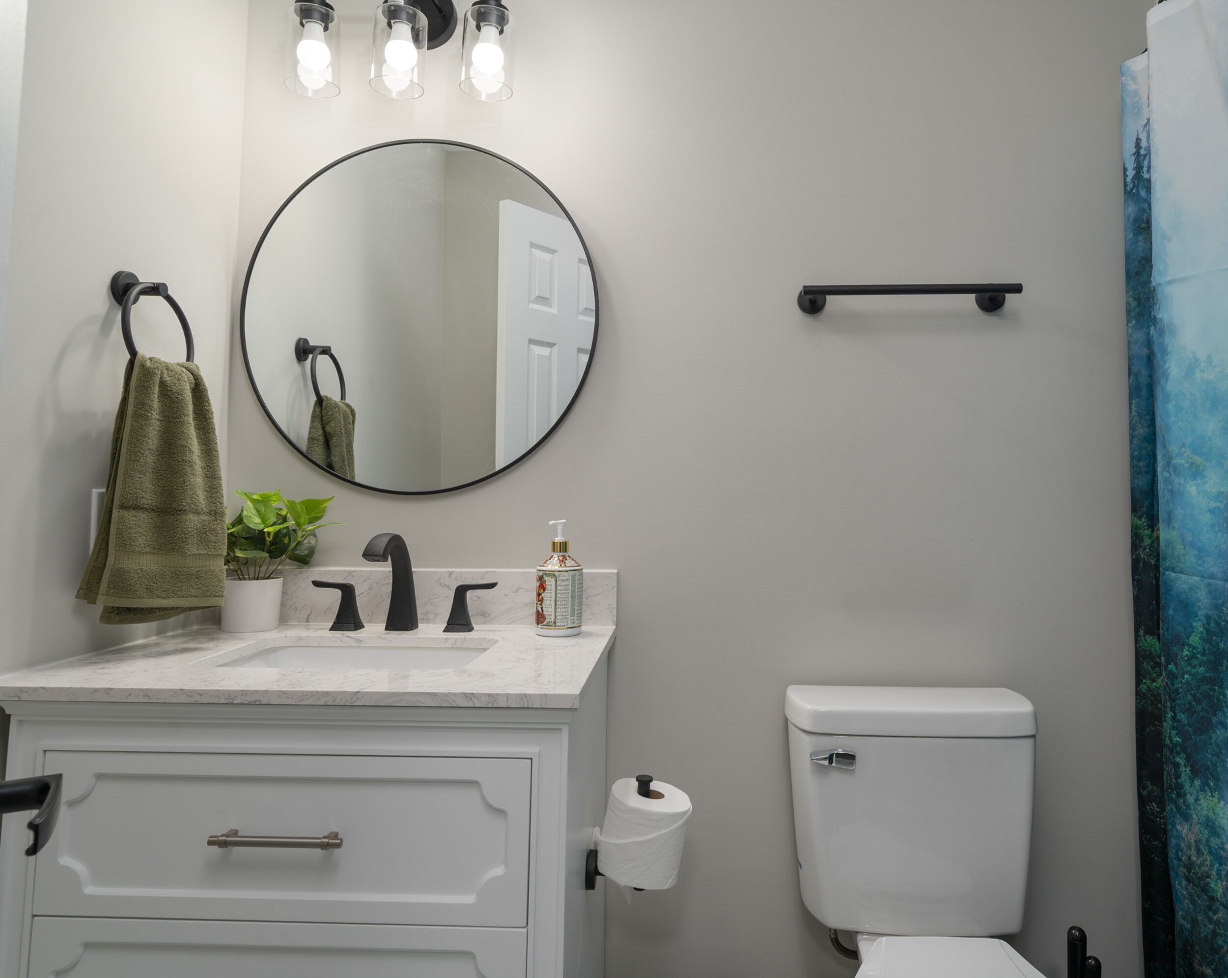 Un bagno con un mobile lavabo bianco, uno specchio rotondo, un WC e una tenda per la doccia.