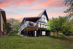 Una casa moderna con un amplio frente de vidrio, un techo inclinado y una terraza de madera.
