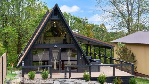 Una casa moderna de color oscuro con techo triangular, un porche cubierto y un camino de piedra que conduce a la entrada.