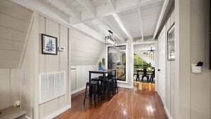 Un pasillo con suelo de madera, paredes blancas y una escalera que lleva a un comedor.