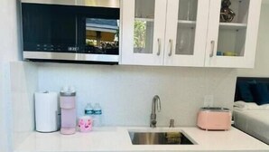 A compact kitchen with white cabinets, a stainless steel dishwasher, and a sink. - Brand New Studio with Pool Access (Oakland Park)