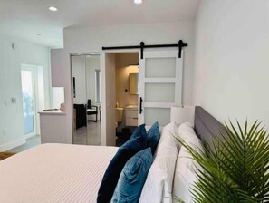A bedroom with a bed, a sliding door leading to a bathroom, and a plant in the corner.