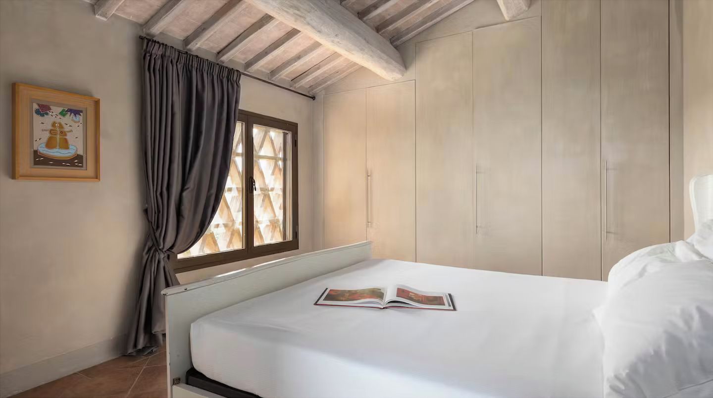 A bedroom with a bed, a window with curtains, a wardrobe, and a framed picture on the wall.