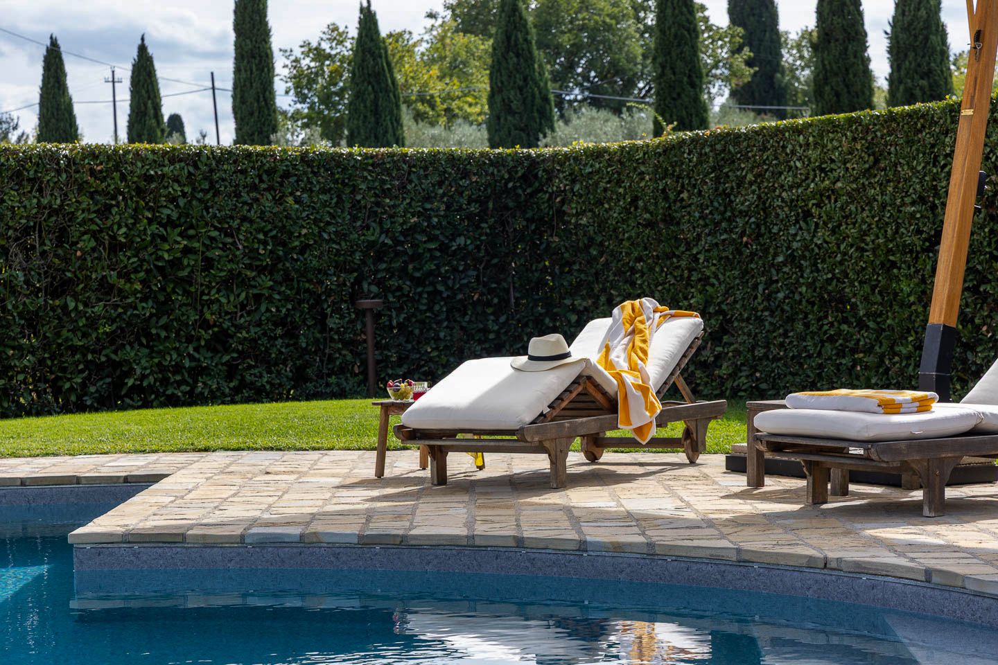 Área ao lado da piscina com espreguiçadeiras e um conjunto de arbustos ao fundo.