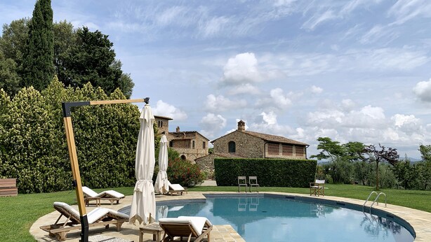 A pool area with lounge chairs and umbrellas, a stone building in the background, and a clear sky.