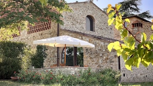 A stone building with a garden, outdoor seating, and a white umbrella.