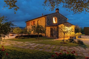 Un bâtiment en pierre doté d’une grande fenêtre en arc de cercle, entouré d’un jardin bien entretenu avec un sentier en pierre.