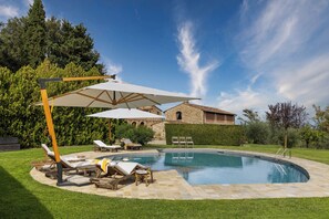 Une piscine entourée de chaises longues et de parasols, avec une pelouse bien entretenue et un bâtiment en pierre en arrière-plan.