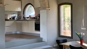 A modern kitchen with an arched doorway, a dining area with a table and chairs, and a window with a view of greenery.