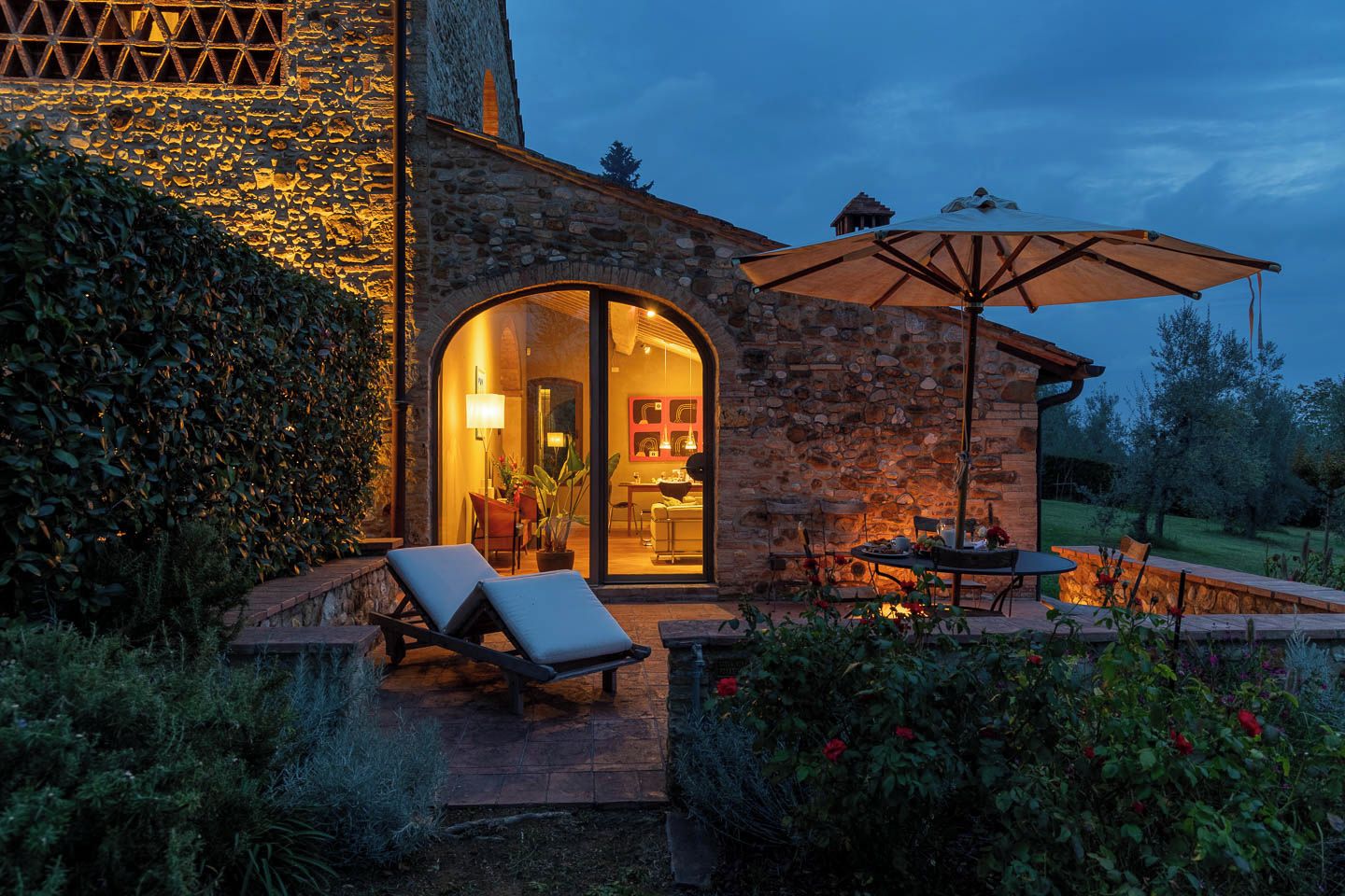 Un edificio de piedra con entrada por una puerta de cristal, mobiliario exterior y un patio.
