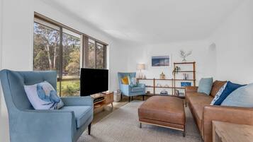 A modern living room with a large window, a blue armchair, a brown sofa, and a wooden side table.