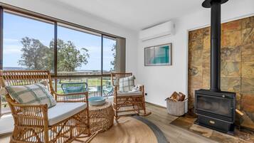 A cozy living room with wicker furniture, a stone fireplace, and a large window overlooking a scenic view.