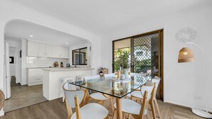 A modern kitchen with white cabinets, a glass-top dining table, and wooden chairs. - Seaglass at Pambula Beach (Pambula Beach)