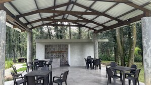 Un patio al aire libre con mesas y sillas, un muro de piedra con diseño de azulejos y una estructura de techo metálico.