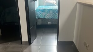 Un pasillo con suelo de baldosas que conduce a un dormitorio con cama y ventana.
