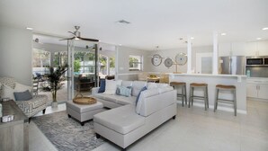 A modern living room with a sectional sofa, a dining area, and a kitchen with bar stools. - Vandy Villas — Walk to Vanderbilt Beach, Pool & Spa (Naples)