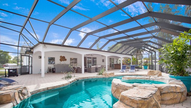 A covered outdoor swimming pool with a patio area, a grill, and a view of the surrounding landscape. - Vandy Villas — Walk to Vanderbilt Beach, Pool & Spa (Naples)