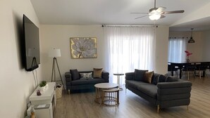 Ein modernes Wohnzimmer mit zwei Sofas, einem Couchtisch, einem an der Wand montierten Fernseher und einem Deckenventilator.