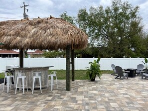Un patio al aire libre con un toldo de paja, una barra de madera y arreglos de asientos.