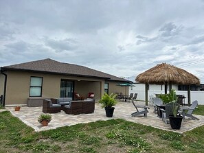 Une maison dotée d’un patio aménagé avec des meubles d’extérieur, une structure à toit de chaume et des plantes en pot.