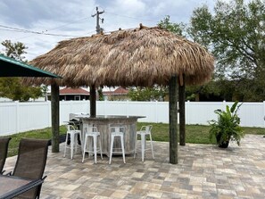Un patio al aire libre con techo de paja, una zona de bar y un conjunto de asientos.