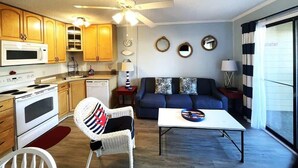 Un espace de vie compact comprenant un coin cuisine, un coin repas et un espace détente avec un canapé et un fauteuil.