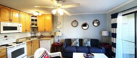 Een compacte leefruimte met kitchenette, een eethoek en een zithoek met een bank en een fauteuil.