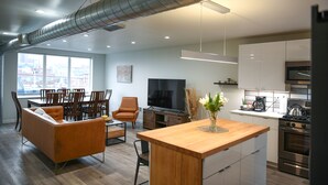 Una cocina moderna con electrodomésticos de acero inoxidable, una isla de madera y un comedor con sofá y sillas.