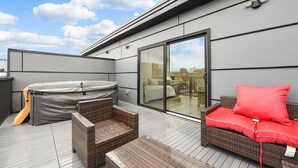 Una terraza en la azotea con jacuzzi, mobiliario de mimbre y puerta de vidrio que da a un espacio interior.