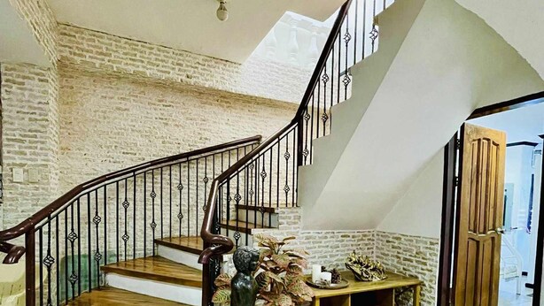 A staircase with a wooden finish and metal railings, leading to a landing area with a wooden bench and a statue. - Cozy vacation home for family in Uptown Cagayan de Oro City Close to everything (Cagayan de oro city)
