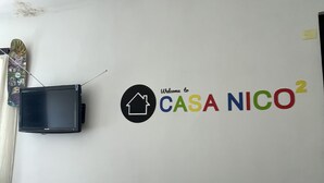 Una pared blanca con un televisor montado y un letrero colorido que dice "Welcome to CASA NICO²".