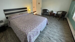 Una habitación de hotel con una cama, una silla, una mesita y una puerta.