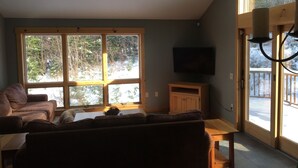 Ein gemütliches Wohnzimmer mit großem Fenster, einem Fernseher und einem Holzschrank.