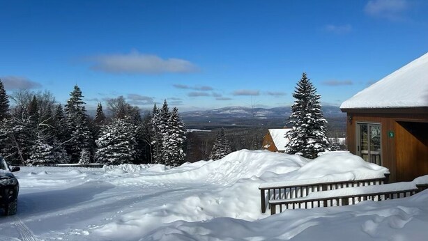 Schneebedeckte Landschaft mit einer Holzhütte und einem geparkten Auto im Vordergrund.