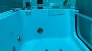 A modern bathroom with a large bathtub, a wine bottle, and two glasses on a vanity.