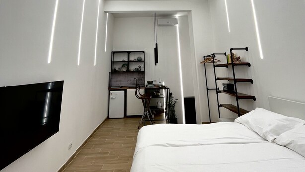 A modern bedroom with a bed, a desk, and a kitchenette.