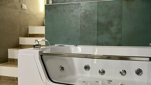 A modern bathroom with a large bathtub, wooden flooring, and a green wall.