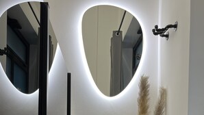 A hallway with a wooden bench, a white vase with pampas grass, and two heart-shaped mirrors with illuminated edges.