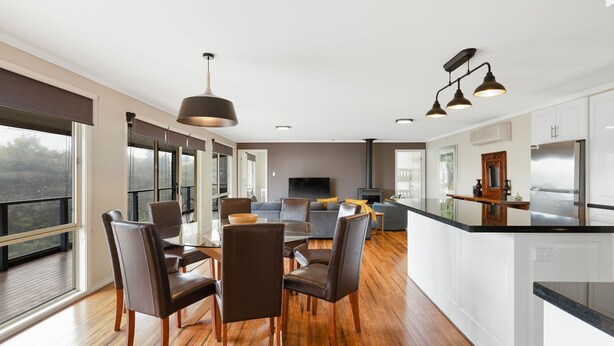 Una cocina moderna con una isla central, comedor con sillas y un ventanal con vistas a un área boscosa.