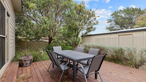 A wooden deck with a table and chairs, surrounded by trees and a fence.