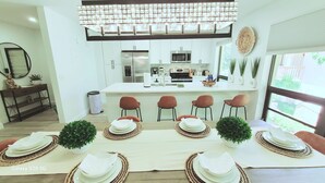 A modern kitchen with white cabinets, a central island, and a dining area set for six with woven placemats and red chairs.