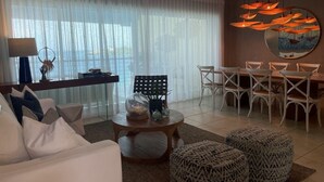 A modern living room with a sofa, coffee table, and ottomans. There is a dining area with chairs and a table. - Beautiful Apartment in Sosua with Maid included (Sosua)